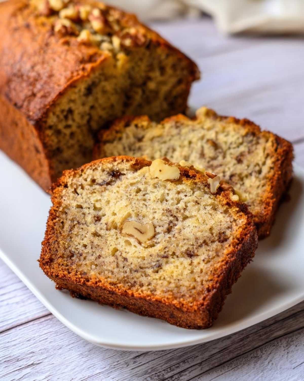 A loaf of golden-brown banana bread with two slices cut and placed in front, showing walnuts and moist texture, perfect for a starbucks banana bread recipe.