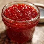 Close-up of a glass jar filled with vibrant red strawberry jam, with the lid slightly open in the background.