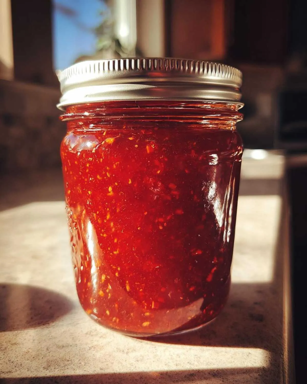 Close-up of a sealed mason jar filled with vibrant red strawberry jam, ready for canning.