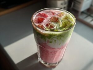Close-up of a glass of strawberry matcha latte with ice and layered pink and green colors.