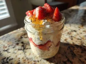 A glass jar filled with overnight oats, layered with sliced strawberries, topped with yogurt, honey, and chia seeds.