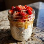 Close-up of overnight oats in a jar, topped with fresh strawberries, chia seeds, and a drizzle of honey.