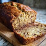 A close-up of a freshly baked loaf of zucchini banana bread with one slice cut, showing moist texture and chocolate chips.