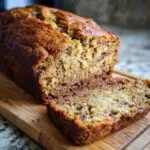 A close-up of a freshly baked loaf of zucchini banana bread with one slice cut, showing moist texture and chocolate chips.