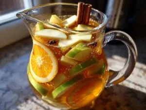 A glass pitcher filled with apple cider sangria, featuring apple slices, orange slices, and cinnamon sticks.