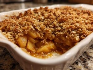 Close-up of a freshly baked apple crisp in a white baking dish with a golden brown oat topping.