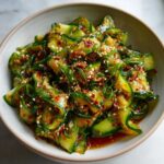 Close-up of a bowl of asian cucumber salad with thinly sliced cucumbers, red chili flakes, and sesame seeds.
