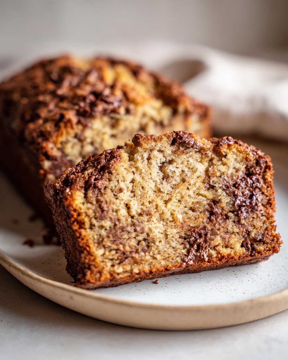 A slice of moist banana bread with melted chocolate swirls on a plate, showcasing the texture.