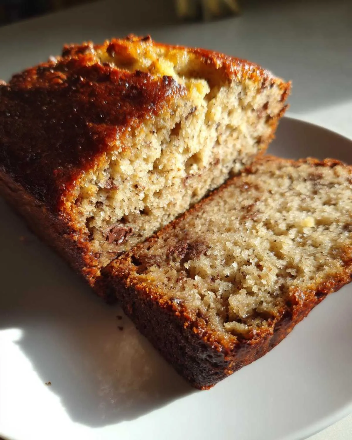 A loaf of ultra-moist banana bread with a slice cut, showing the texture and chocolate chips.