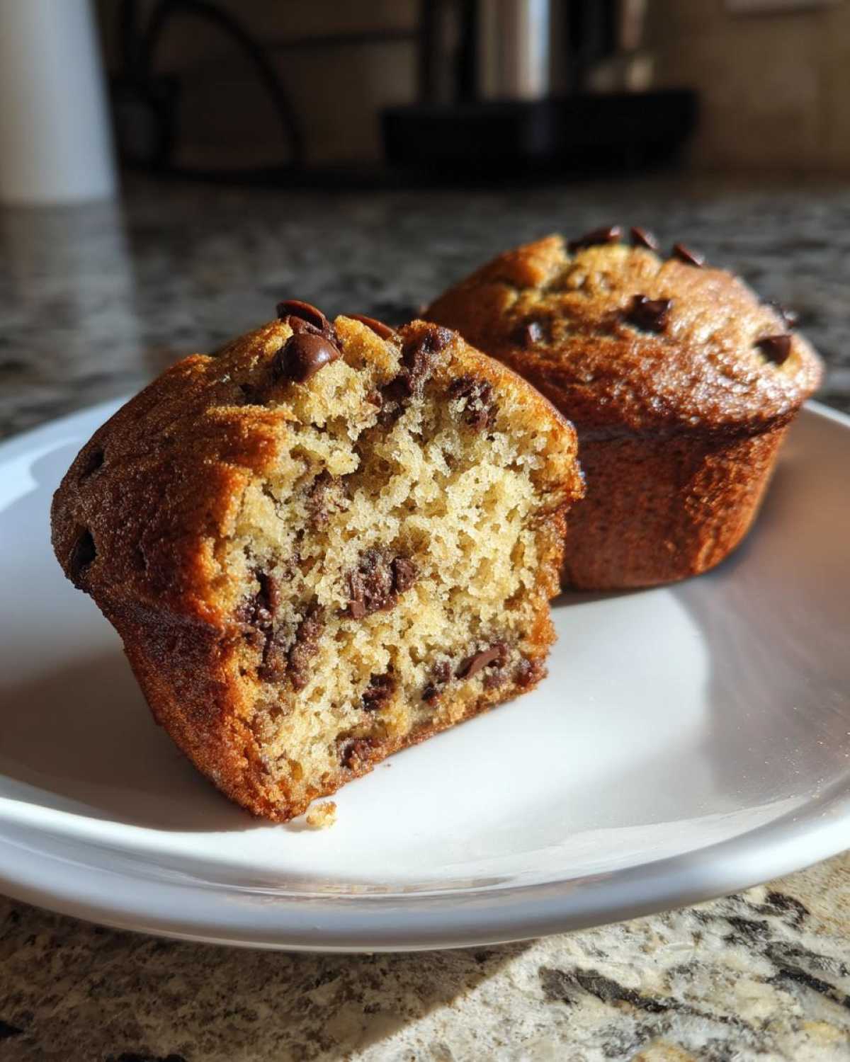 Close-up of a halved banana protein muffin showing the moist interior with chocolate chips, next to a whole muffin.
