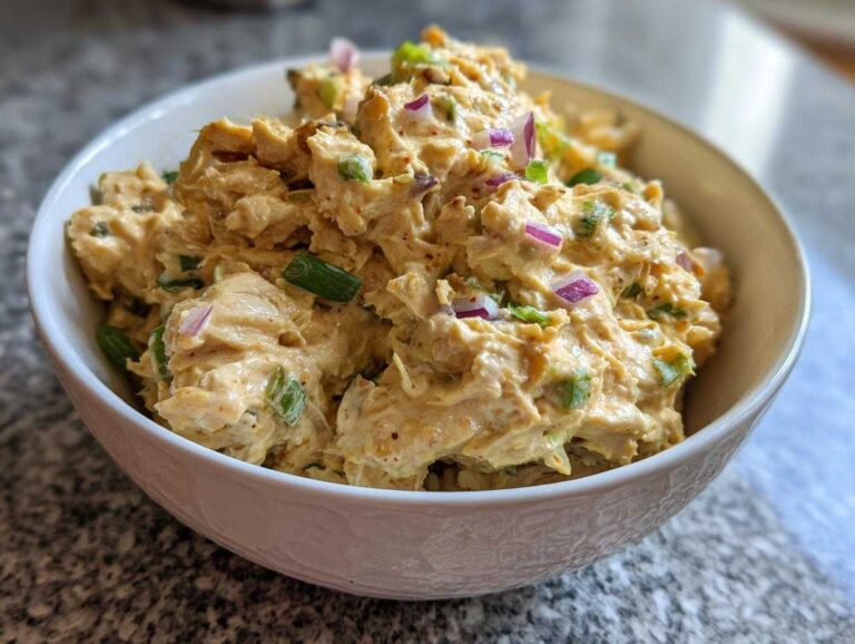 Close-up of a white bowl filled with creamy chickpea tuna salad, garnished with chopped red onion and green onions.