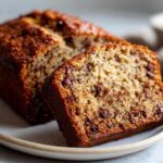 A slice of moist banana bread with chocolate chips on a plate, showcasing its texture and deliciousness.