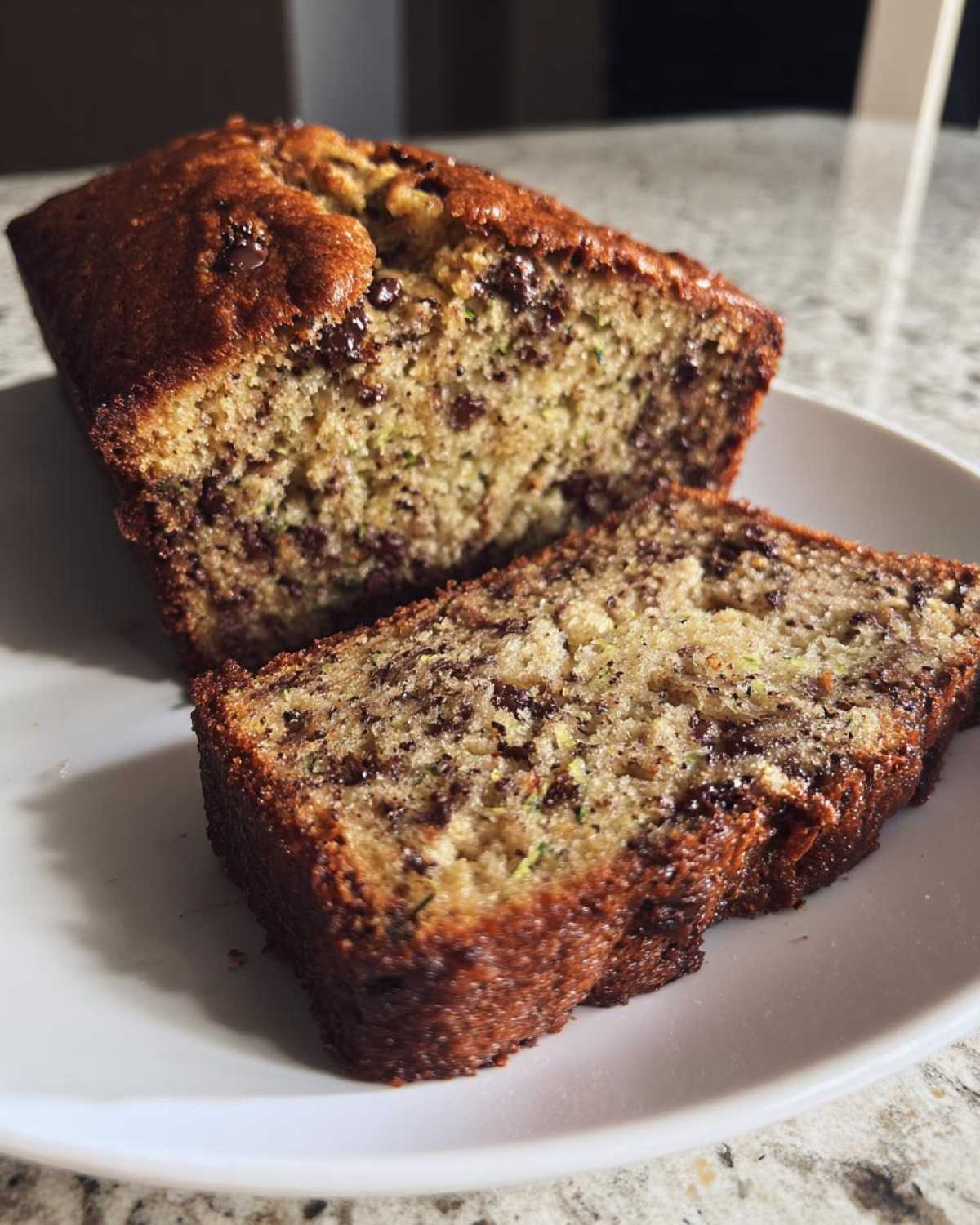 Freshly baked zucchini bread loaf with chocolate chips, sliced on a white plate.