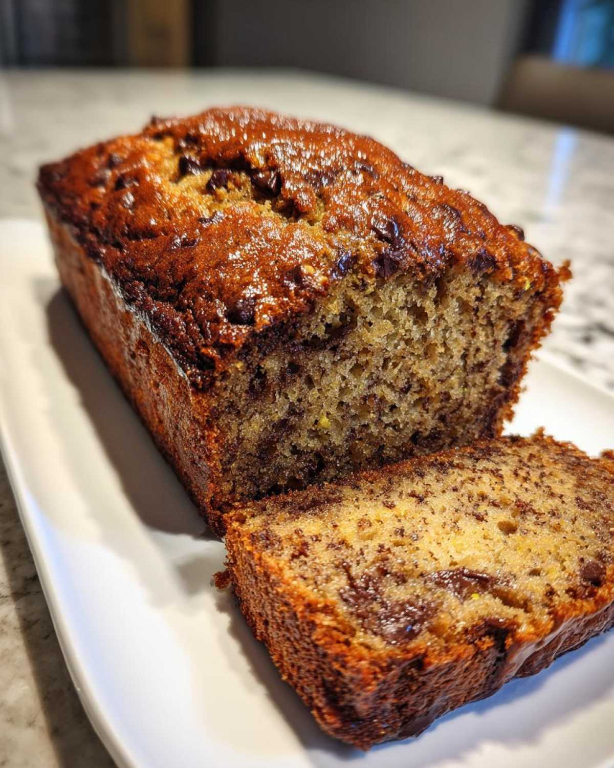 A freshly baked loaf of zucchini bread with chocolate chips, with a slice cut and displayed on a white plate.