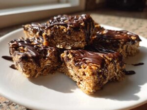 Close-up of several homemade protein bars with a chocolate drizzle on a white plate, showing the texture of oats and nuts.