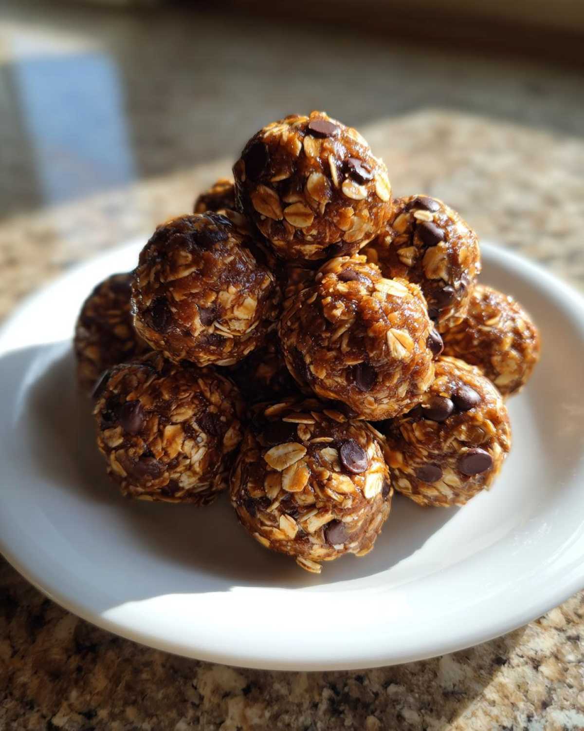 A close-up of a stack of chocolate peanut butter protein bites on a white plate, showing oats and chocolate chips.