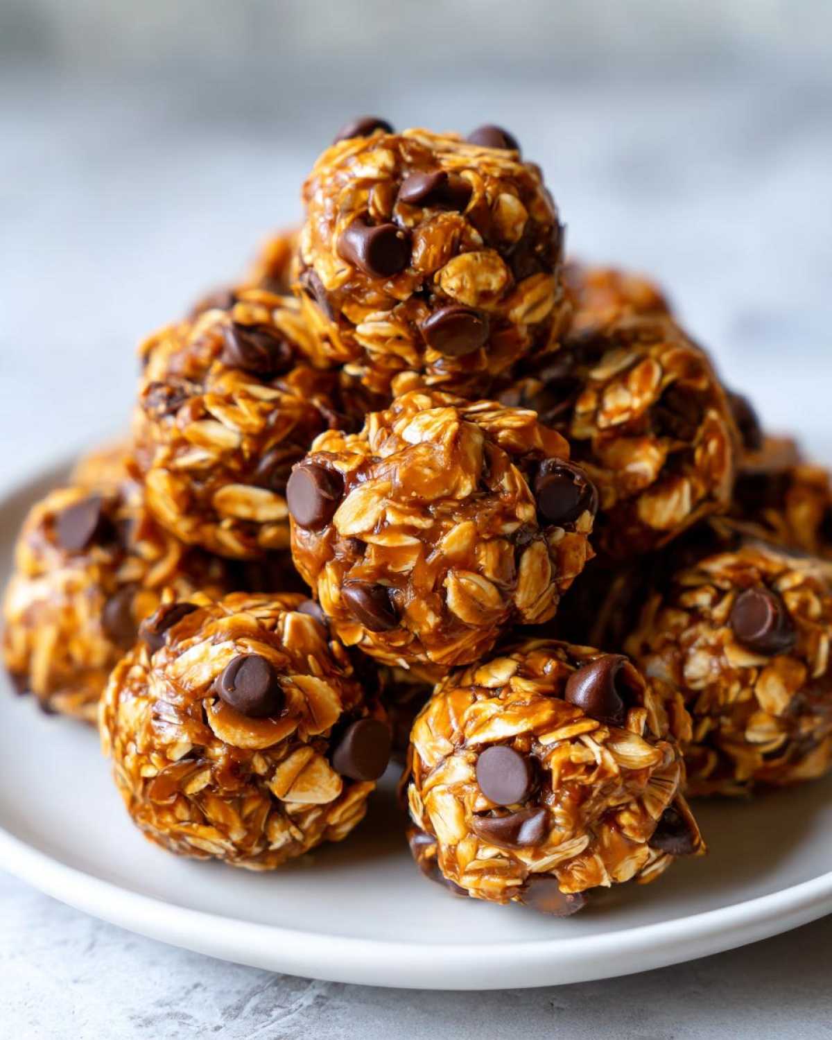 A close-up stack of chocolate peanut butter protein bites on a white plate, showing oats and chocolate chips.