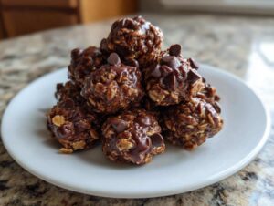A close-up of a stack of chocolate peanut butter protein bites on a white plate, topped with chocolate chips.