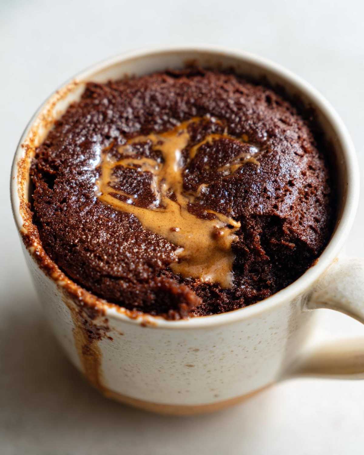 Close-up of a rich chocolate protein mug cake with a swirl of melted peanut butter on top, in a ceramic mug.