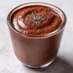 Close-up of a glass filled with rich chocolate protein pudding, topped with a sprinkle of chia seeds.