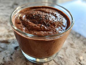 Close-up of rich chocolate protein pudding in a glass cup, topped with chia seeds.