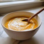Bowl of creamy fall soup with a swirl of cream and a wooden spoon.