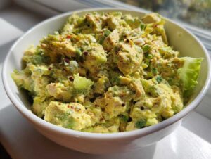 A close-up of a white bowl filled with creamy tuna and avocado salad, garnished with red pepper flakes.