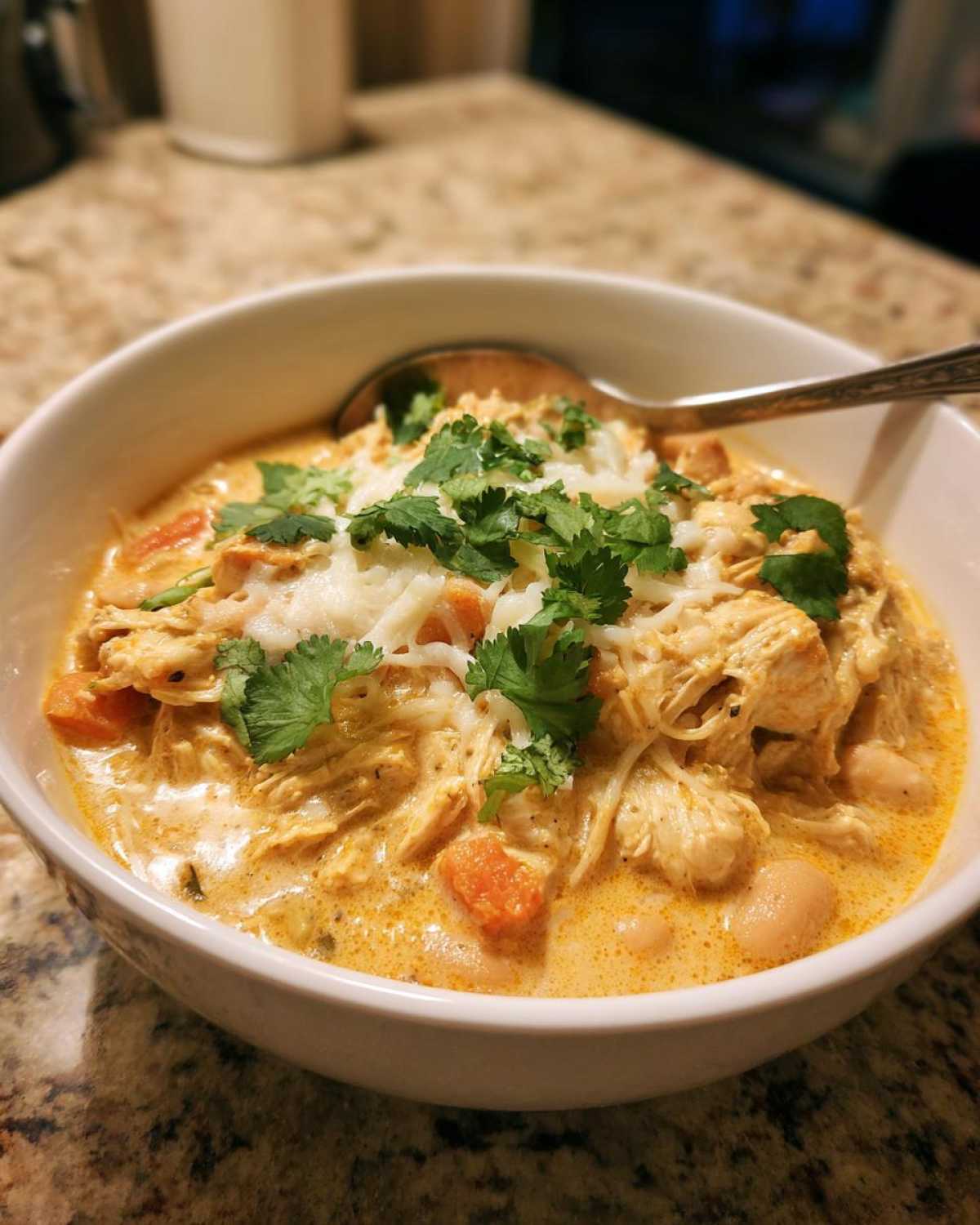 A bowl of creamy white chicken chili topped with cheese and cilantro, ready to eat.