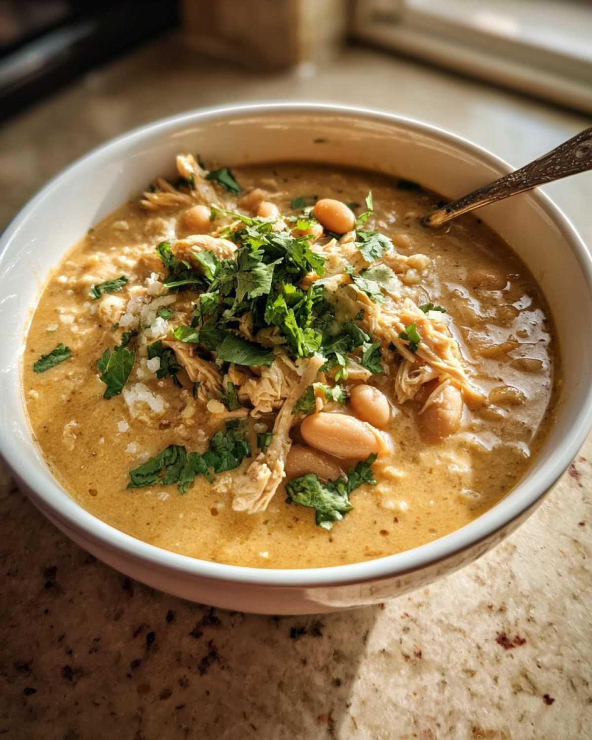 A bowl of creamy white chicken chili topped with shredded chicken, white beans, cilantro, and cheese.