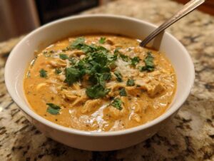 A bowl of creamy white chicken chili topped with cilantro and cheese, ready to eat.