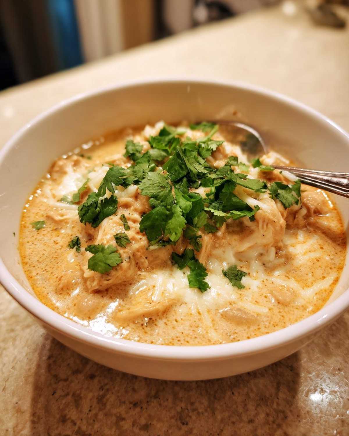 A bowl of creamy white chicken chili topped with cheese and cilantro, ready to eat.