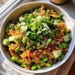 A vibrant bowl of crispy rice salad with edamame, cucumber, carrots, and fresh herbs.
