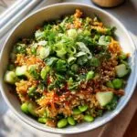 A vibrant bowl of crispy rice salad with edamame, cucumber, carrots, and fresh herbs.