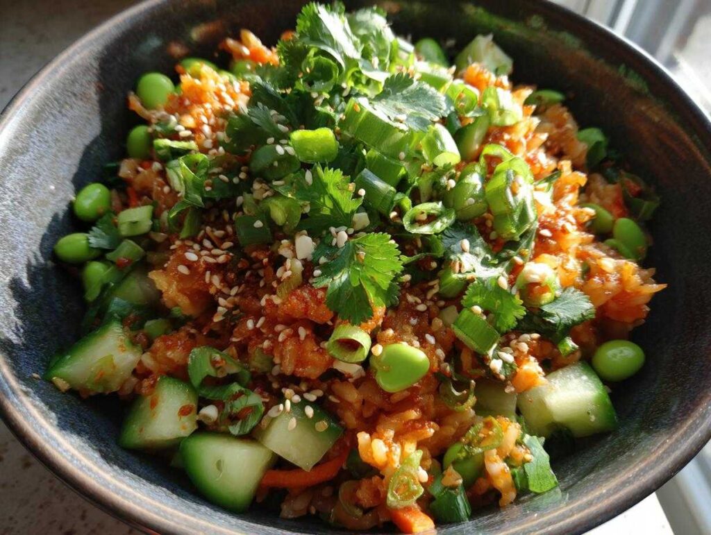 A vibrant bowl of crispy rice salad, topped with cilantro, green onions, edamame, cucumber, and sesame seeds.