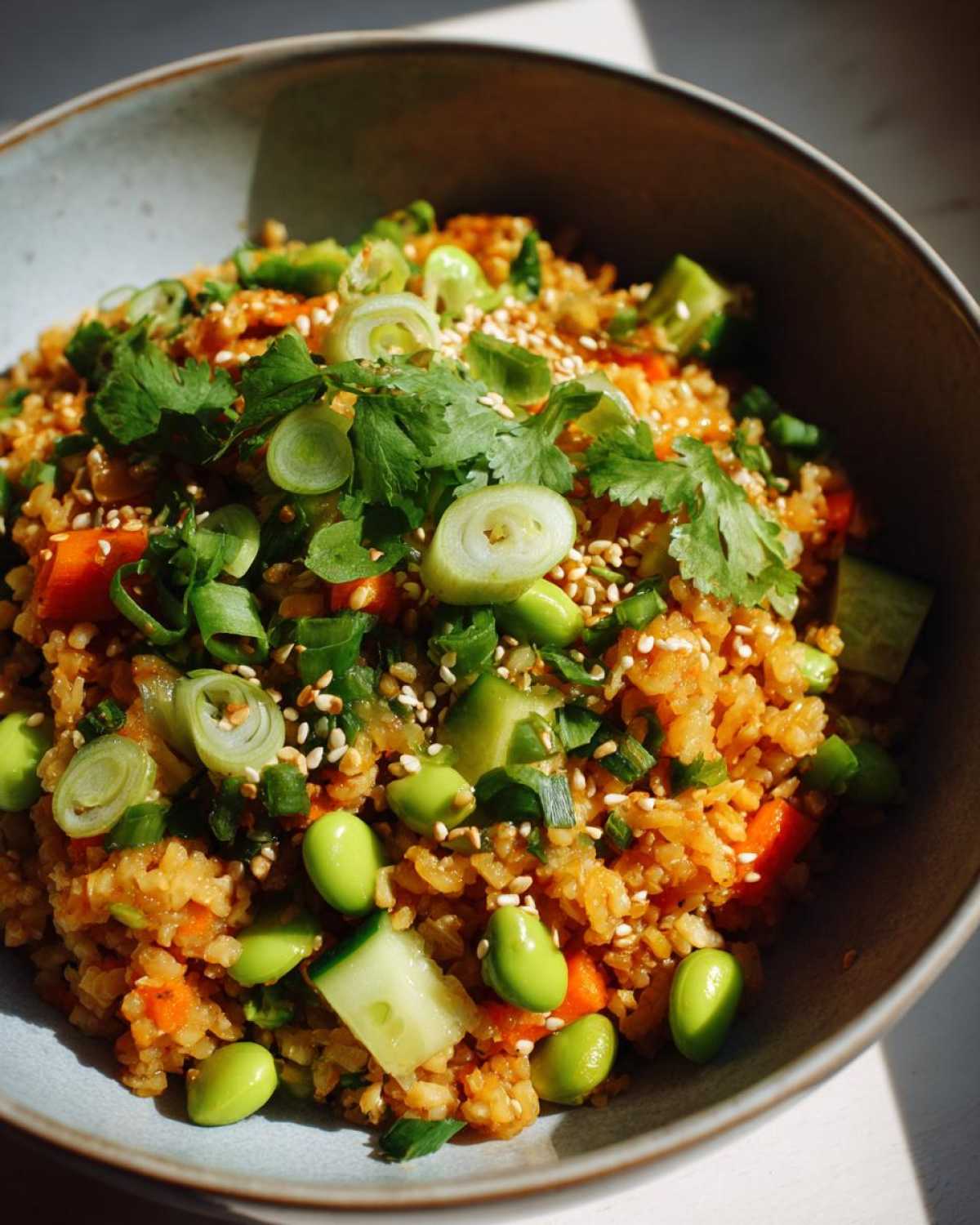 A vibrant bowl of crispy rice salad with rice, edamame, cucumber, carrots, and herbs.