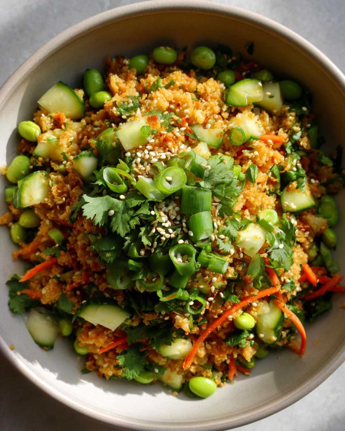 Overhead shot of a vibrant crispy rice salad bowl, featuring rice, cucumbers, edamame, carrots, and garnished with fresh herbs.