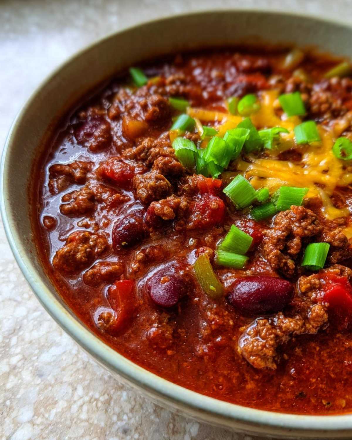 Close-up of a bowl of crockpot chili, topped with shredded cheese and green onions.