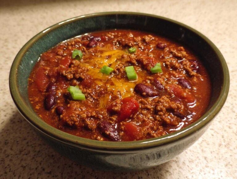 A bowl of crockpot chili with kidney beans, tomatoes, ground beef, cheese, and green onion garnish.