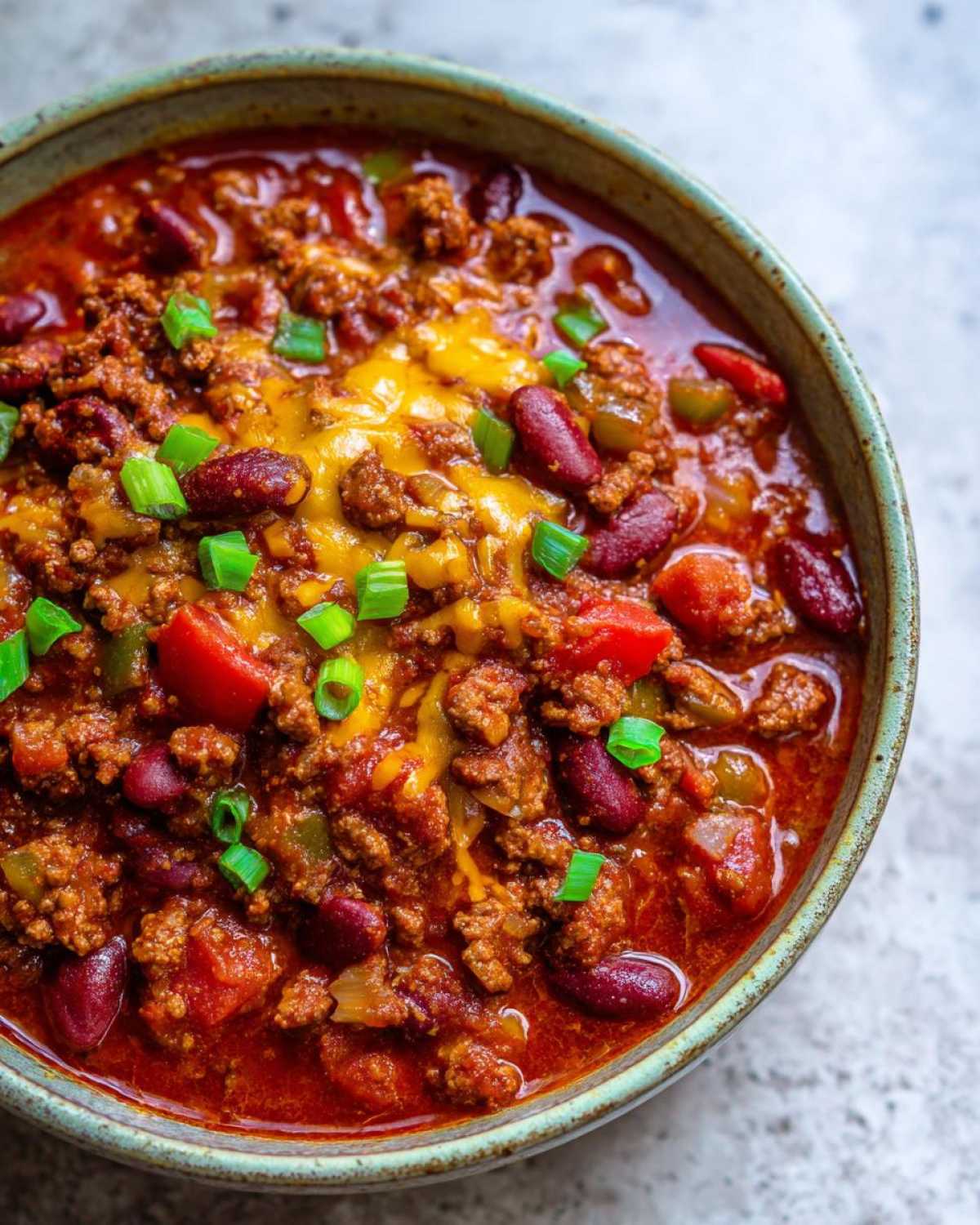 Overhead view of a bowl of crockpot chili topped with melted cheese and green onions.