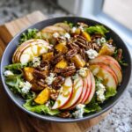 A vibrant fall salad featuring sliced apples, pecans, crumbled cheese, and a maple dressing.