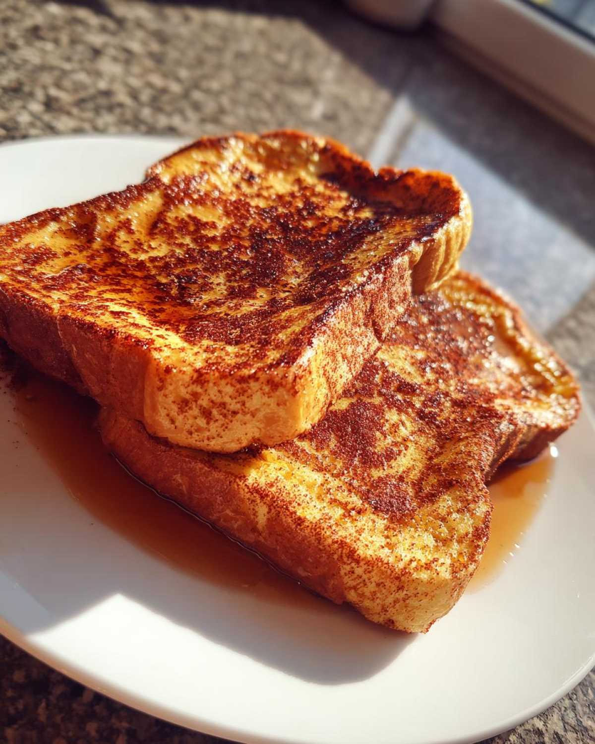 Two slices of golden-brown protein french toast, drizzled with maple syrup and sprinkled with cinnamon, on a white plate.