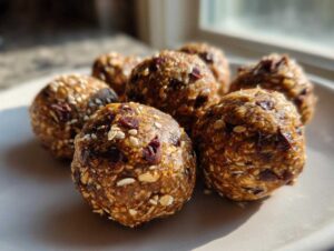Close-up of several healthy protein balls on a plate, showing texture with oats, sesame seeds, and dried cranberries.