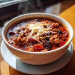 A bowl of hearty chili topped with shredded cheese, featuring kidney beans and ground meat.