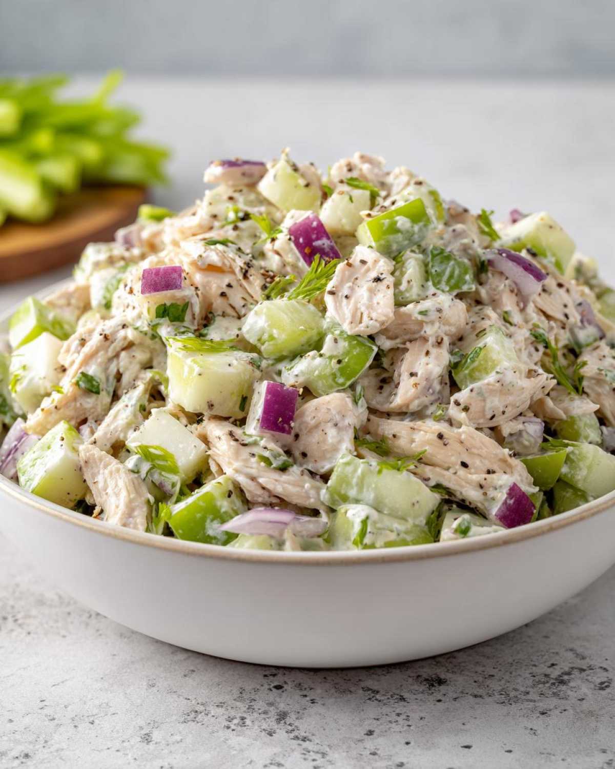 A close-up shot of a bowl filled with high protein chicken salad, featuring chicken, red onion, celery, and green apple pieces.