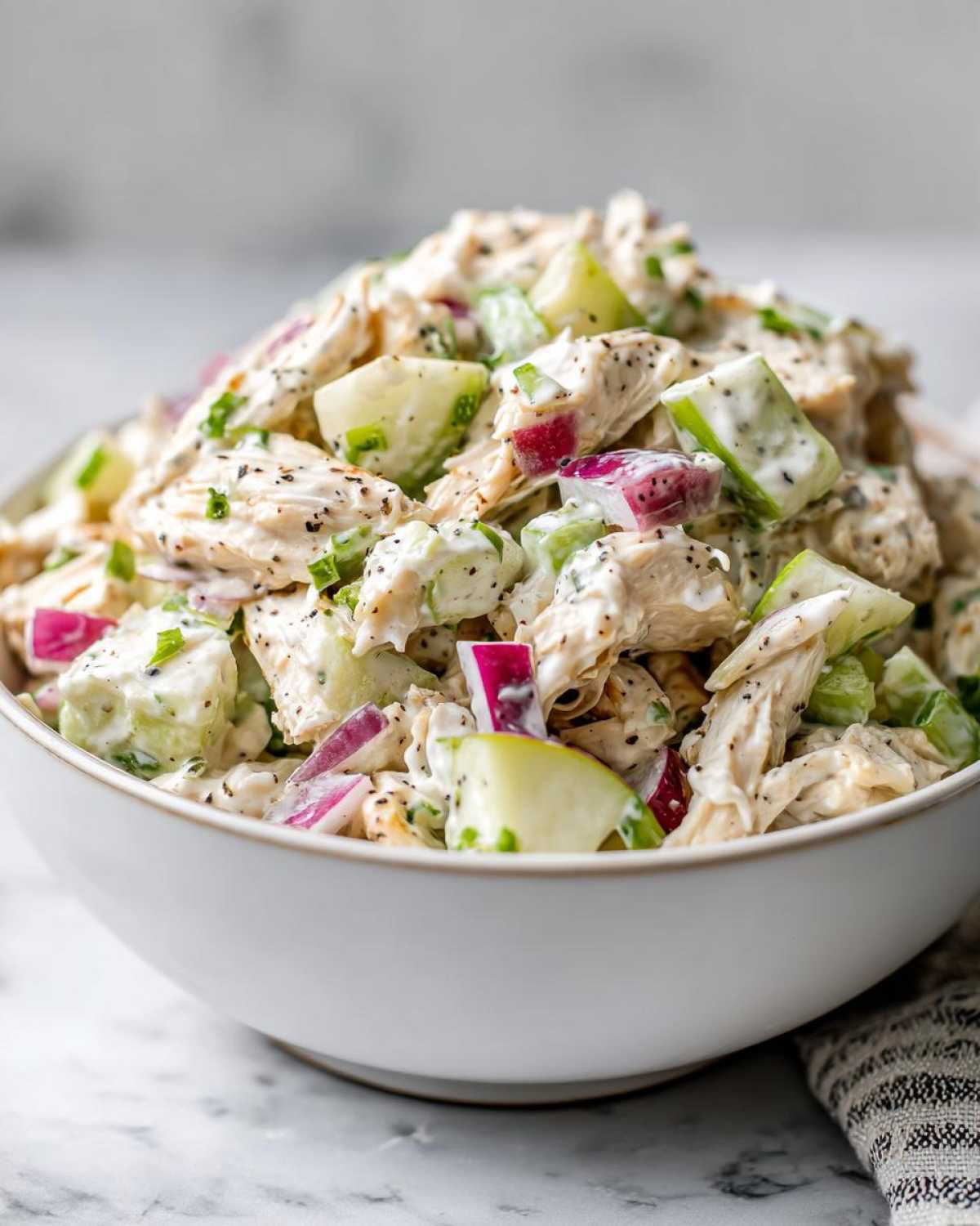 Close-up of a white bowl filled with high protein chicken salad, showing chunks of chicken, red onion, and green apple.