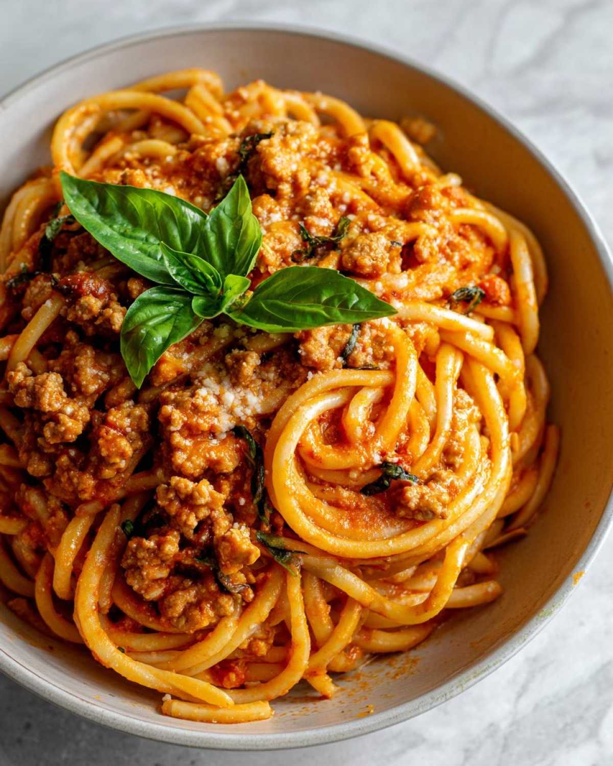 Close-up of a bowl of high protein pasta with a rich meat sauce, grated cheese, and fresh basil leaves.