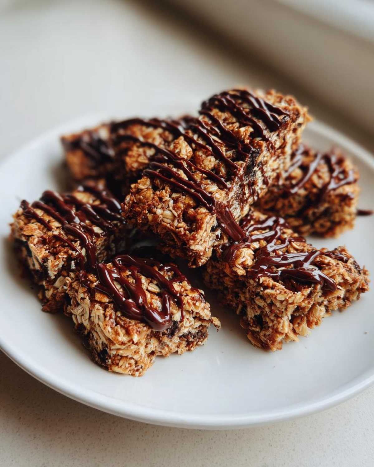 Close-up of several homemade protein bars drizzled with chocolate, on a white plate.