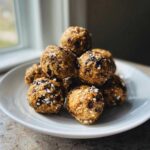 A close-up of a pile of homemade protein balls healthy, made with oats and chocolate chips, on a white plate.