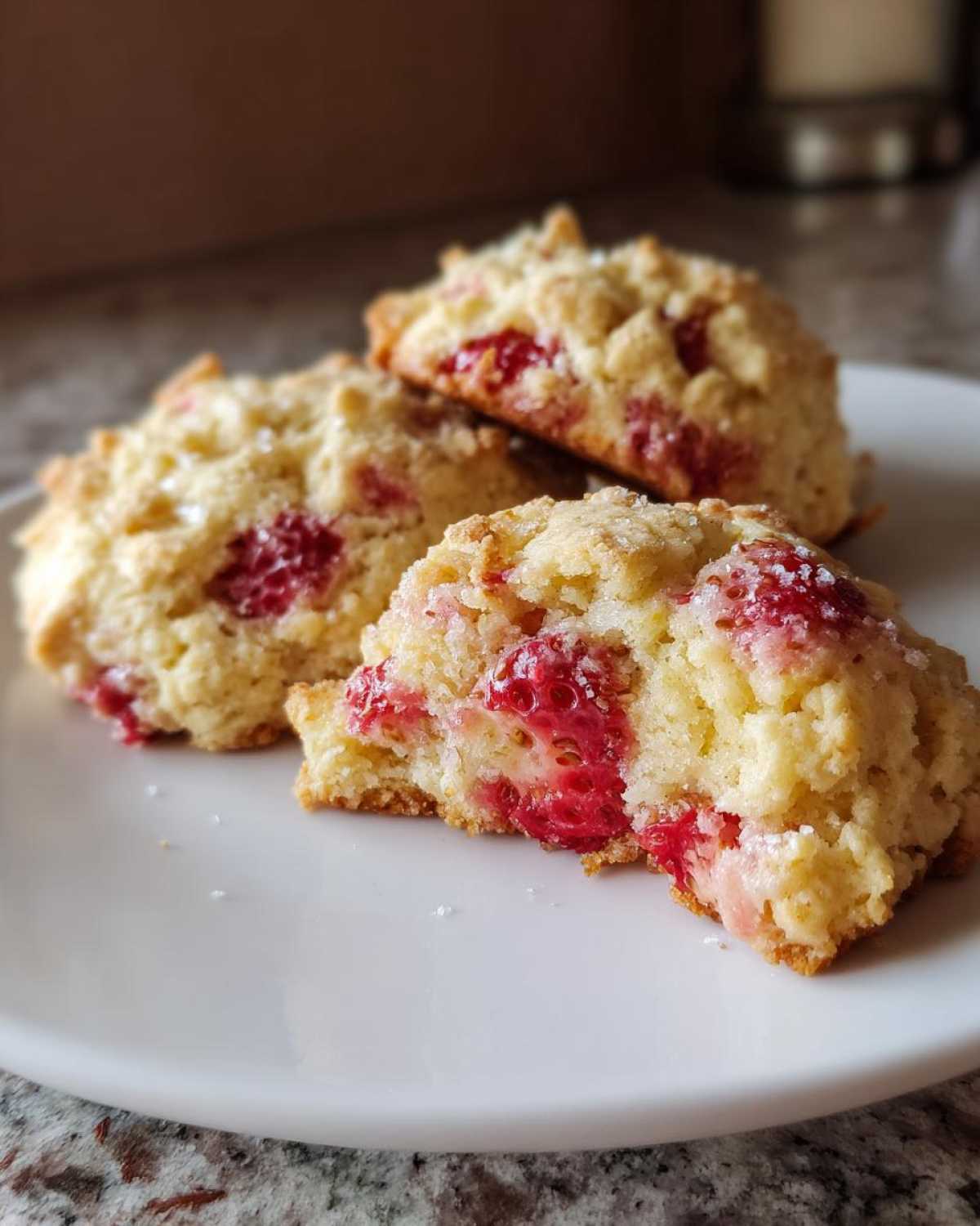 Close-up of three strawberry shortcake cookies on a white plate, one broken open to show the juicy strawberry pieces inside.