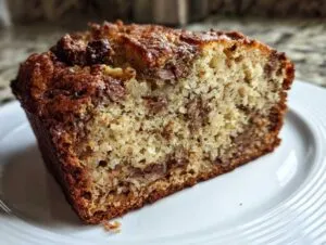A slice of moist banana bread on a white plate, showcasing its texture and ingredients.